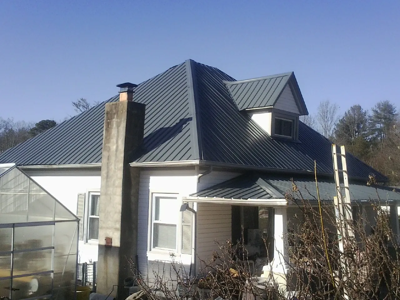 Dark blue standing seam metal roof on a white farmhouse with dormer — Slate & Tile Roof Repair by Roofing Brothers in Matteson