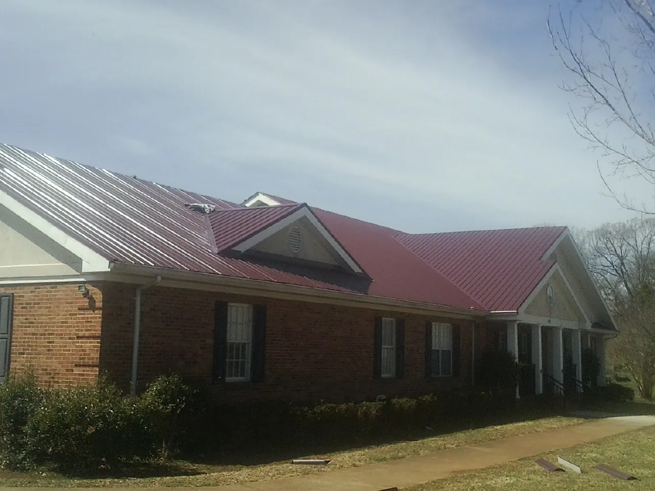 Red metal roof with gabled entries on a long brick building, from a Hail Damage Roof Repair job in Matteson