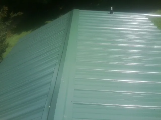New green metal panels meeting at the ridge of a roof — Flat Roof Repair work by our crew in Matteson