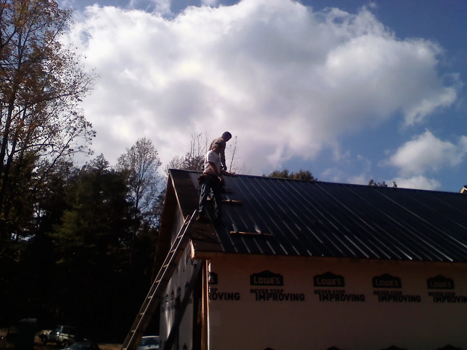 Roofer fastening dark metal panels high against a cloudy sky, from a Roof Inspection job in Matteson